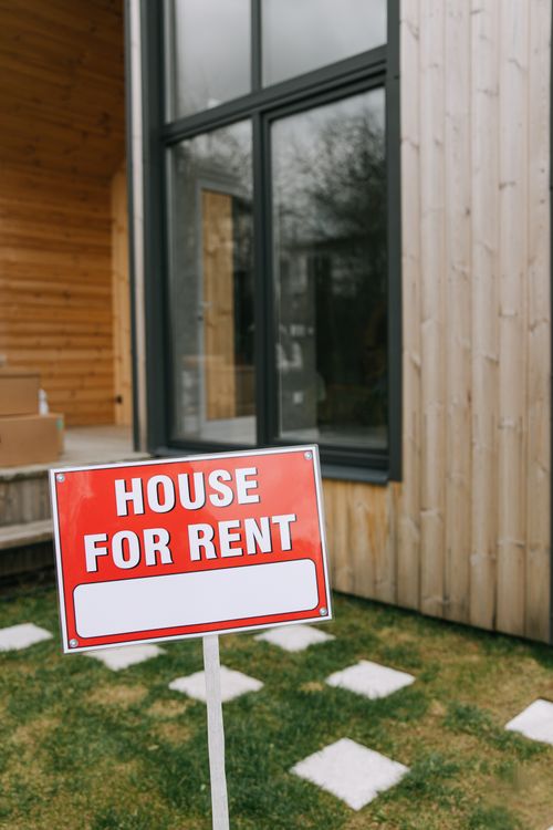 Free A modern wooden house with a bold 'House for Rent' sign on a grassy lawn, showcasing rental opportunity. Stock Photo
