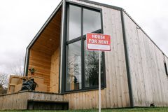 Low-angle view of a modern wooden house with a 'House for Rent' sign, showcasing contemporary architecture.