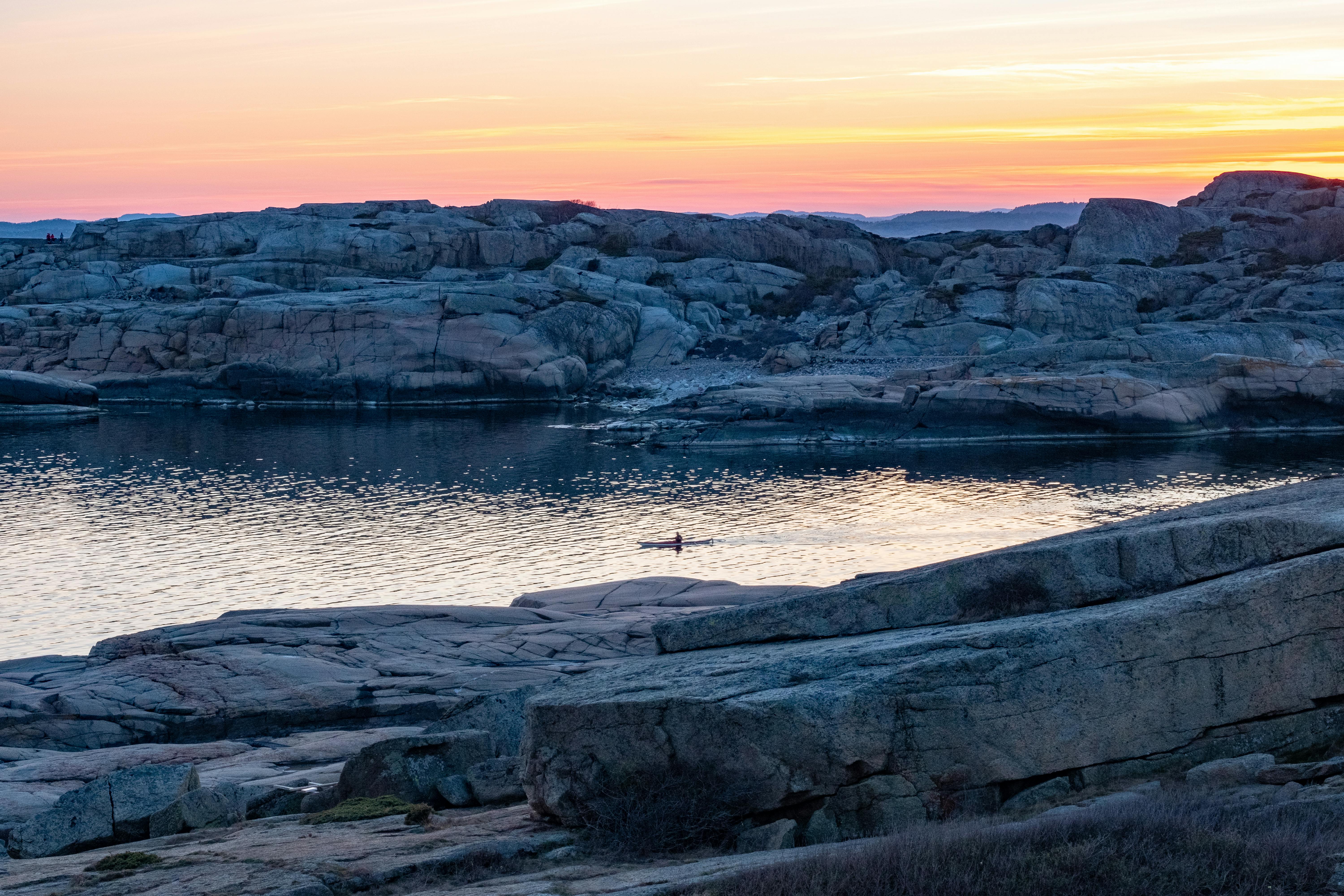 A lone kayaker glides through calm waters at sunset amidst rugged rocky terrain.