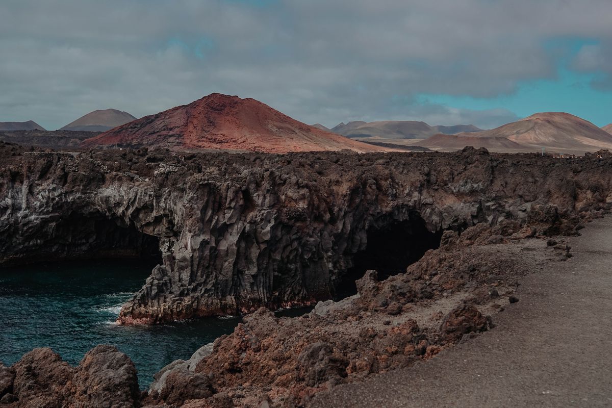 Falezele vulcanice de la Los Hervideros din Lanzarote, cu munți roșiatici în fundal
