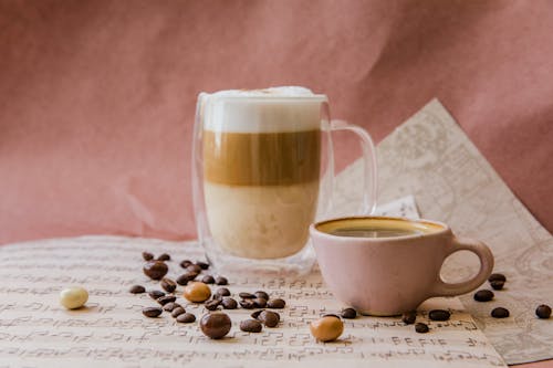 Two Mugs of Coffee with a Milk Foam with Coffee Beans around