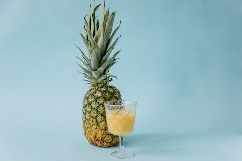 A Glass of Juice beside a Pineapple on a Blue Surface