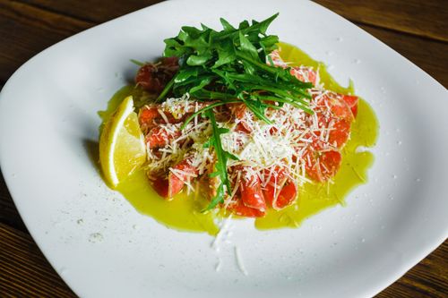 Free Salmon carpaccio garnished with arugula, cheese, lemon, and olive oil. Stock Photo
