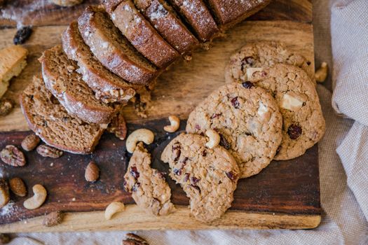 Close-up of sliced bread and cookies with nuts on a rustic wooden board.