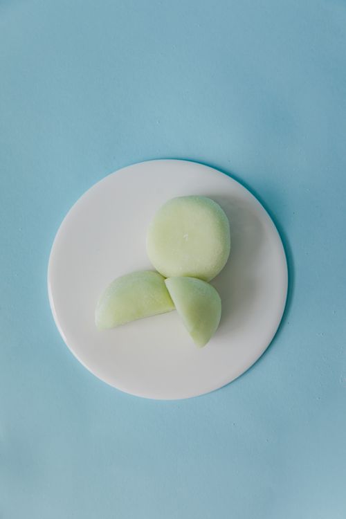 Free Overhead shot of green mochi on white plate with blue backdrop. Stock Photo