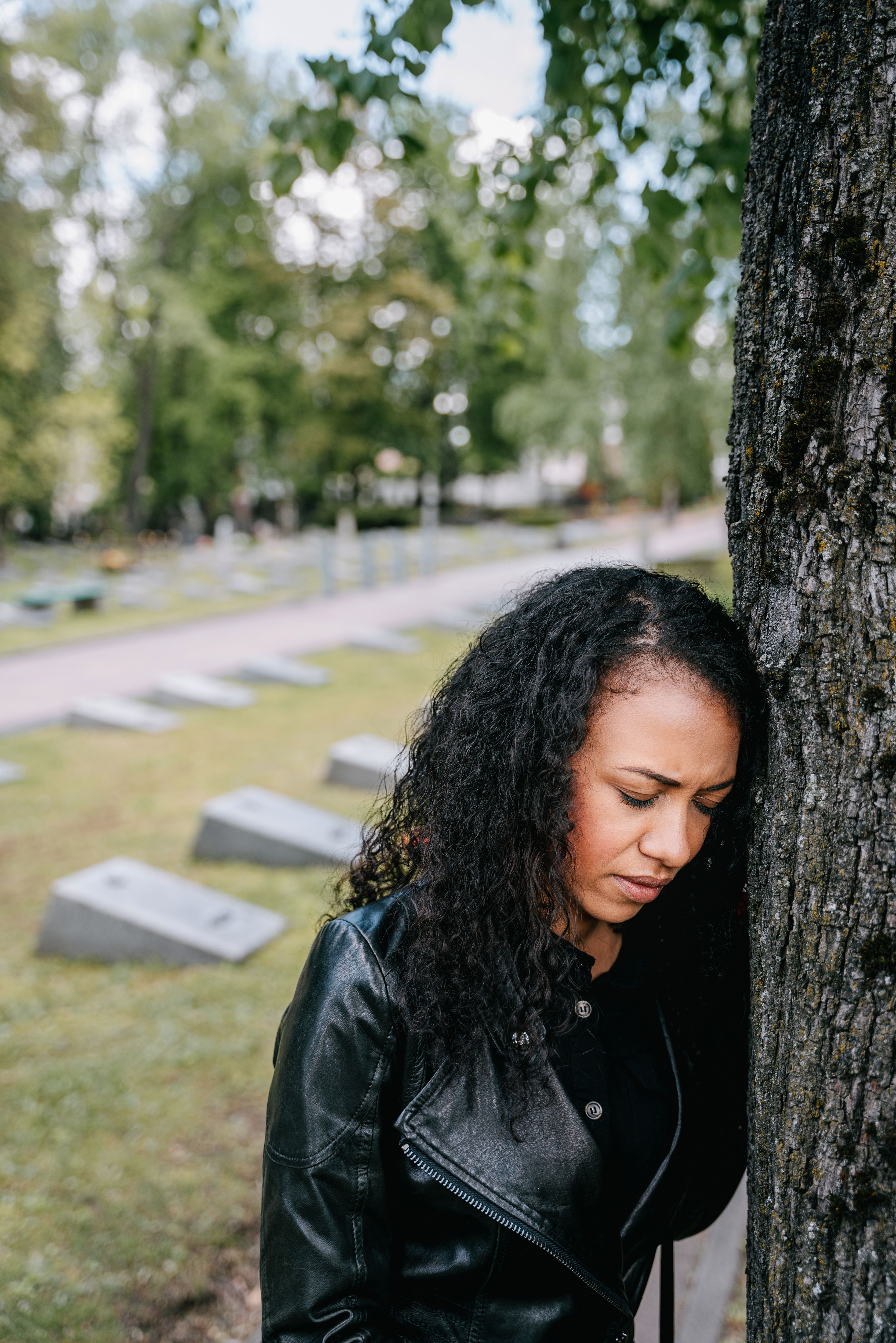 Woman in Black Leather Jacket Standing Beside Tree Trunk · Free Stock Photo