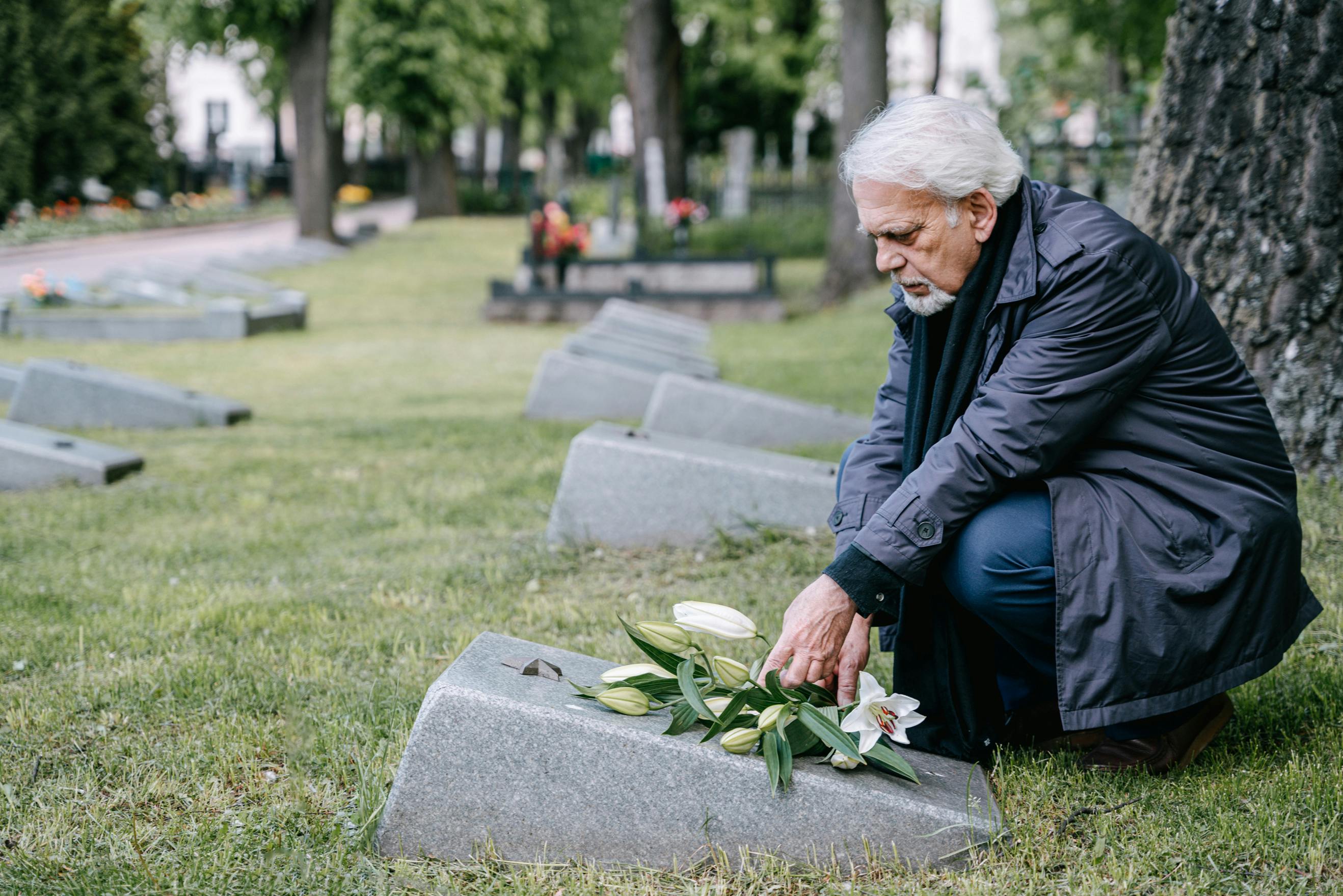 shallow focus of an elderly man in black leather jacket sitting on the grave