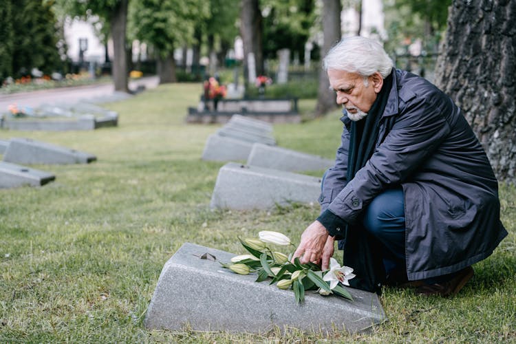 Shallow Focus Of An Elderly Man In Black Leather Jacket Sitting On The Grave