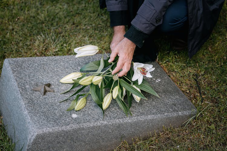 A Person Putting Flowers On A Headstone