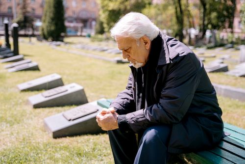 Free Senior man sitting thoughtfully on a bench in a cemetery, reflecting on memories. Stock Photo