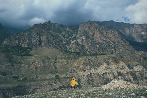 Free A lone hiker in a yellow jacket journeys through dramatic rocky mountains under a cloudy sky. Stock Photo