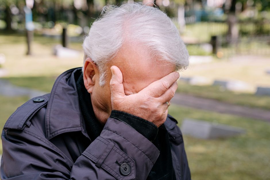 悲しみに暮れる高齢男性が手で顔を覆い、墓地の設定で。