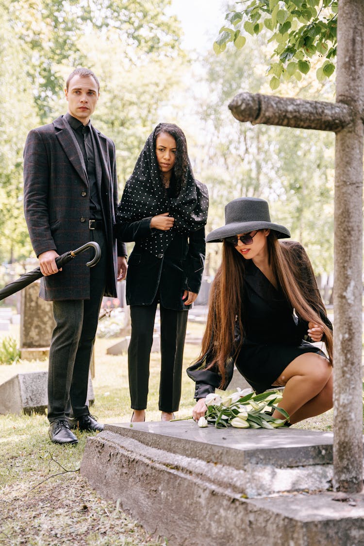 A Family Wearing Black Clothes While Standing Near The Gravestone