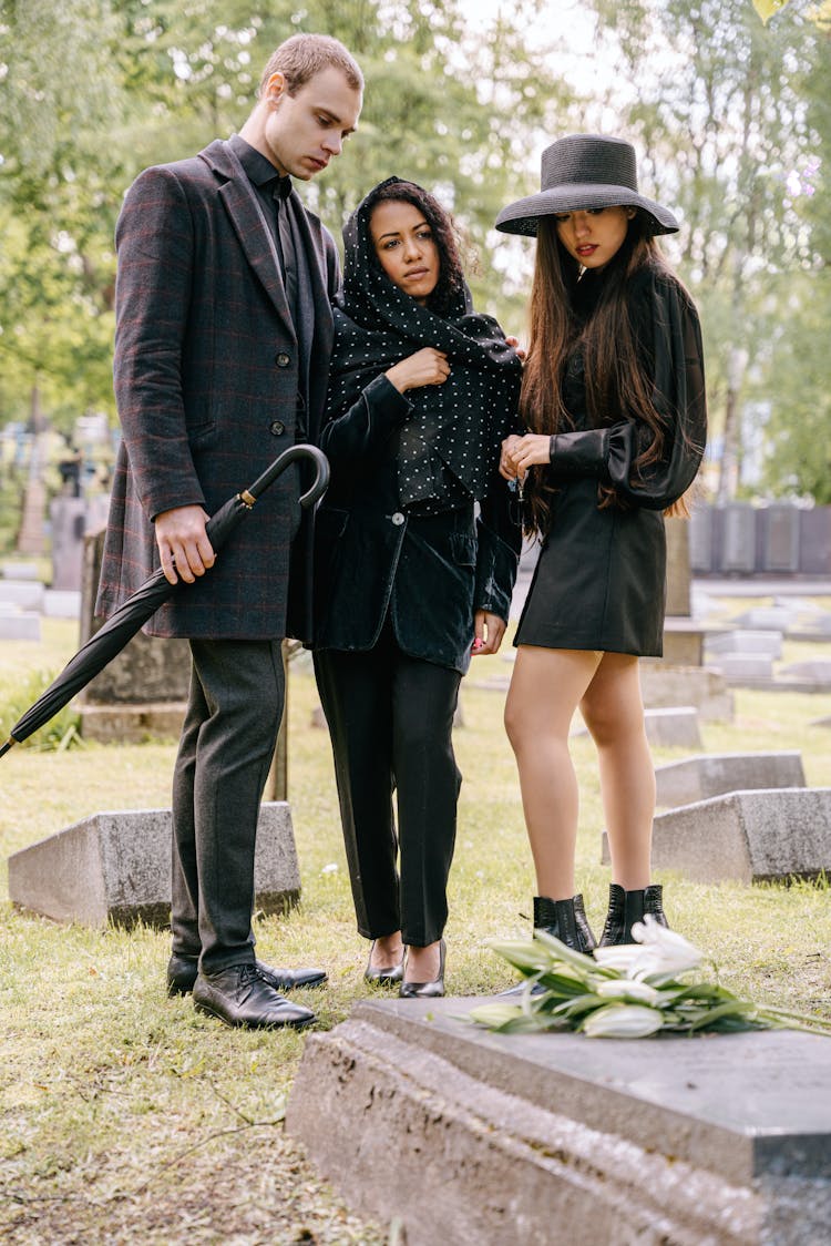 People In Black Outfits Standing By A Grave