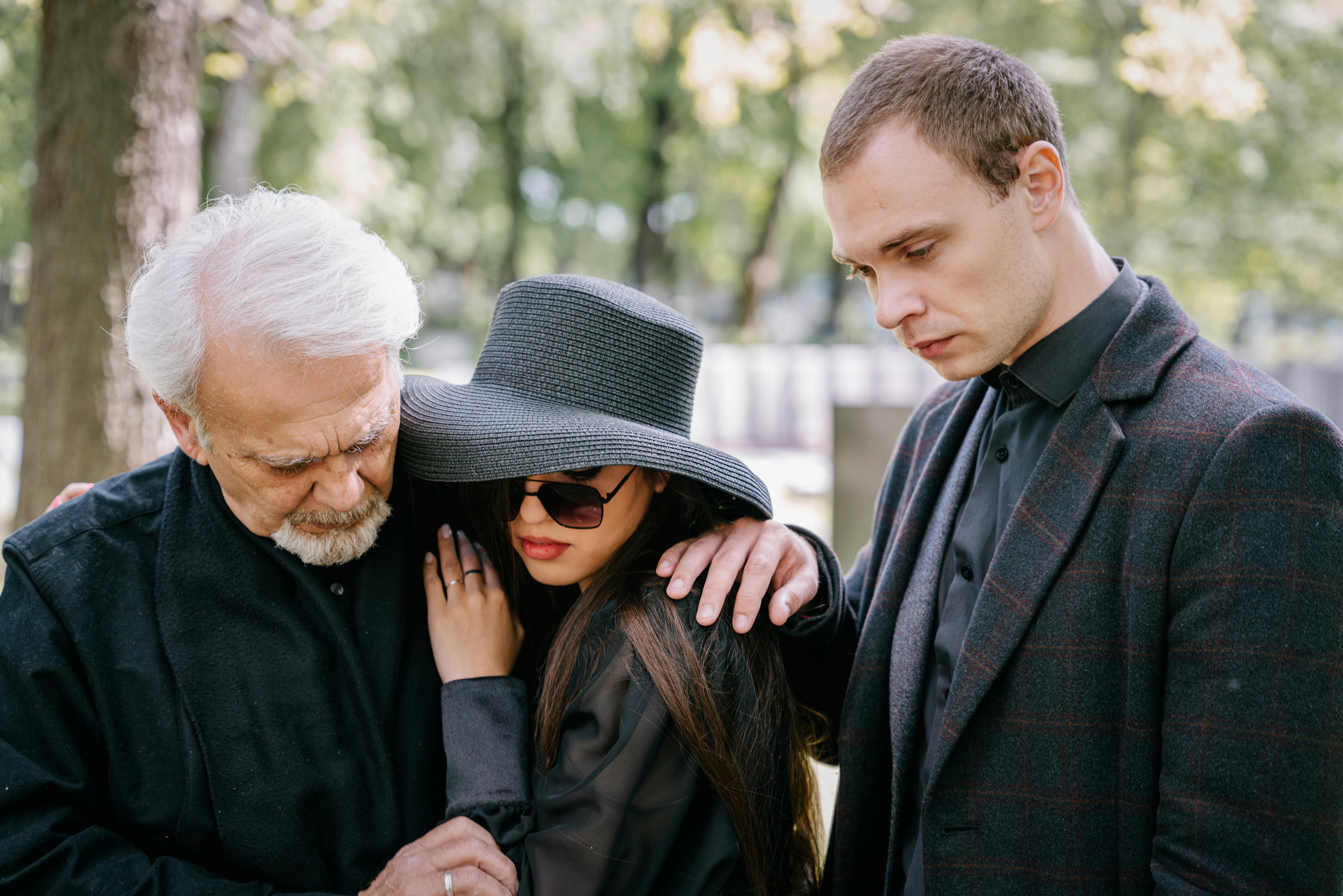 A group of adults in black clothing grieving together outdoors, conveying feelings of loss and sadness.