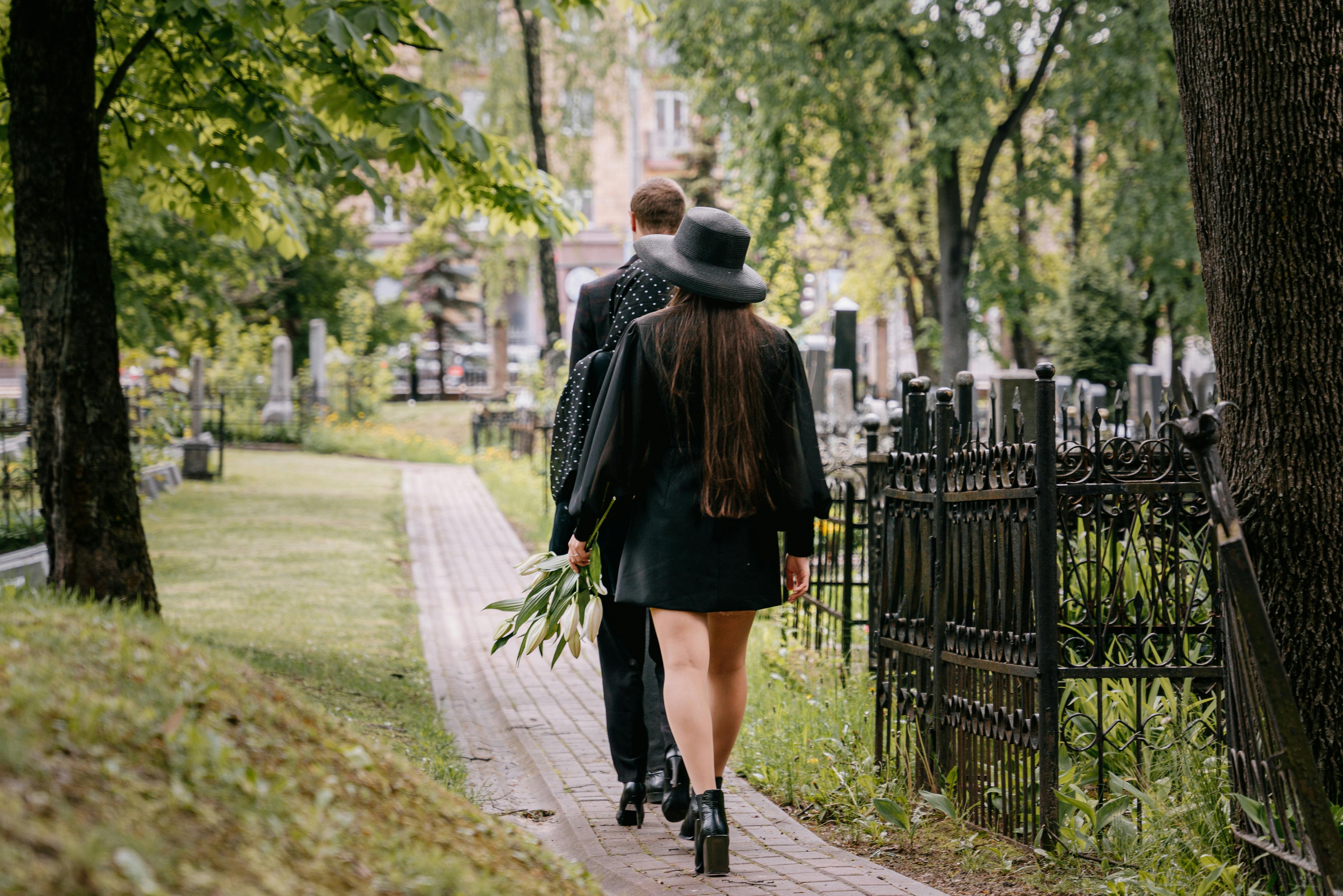 A couple walking through a cemetery, holding flowers in a solemn moment.