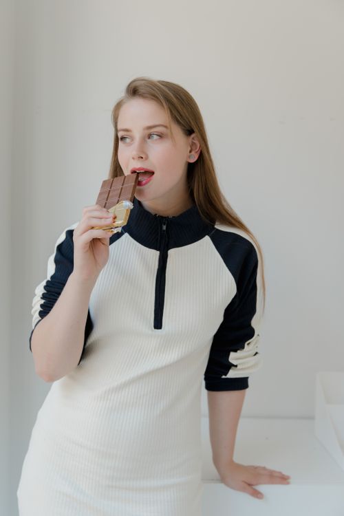 Free A woman in casual attire savoring a chocolate bar in a bright, minimalist room. Stock Photo