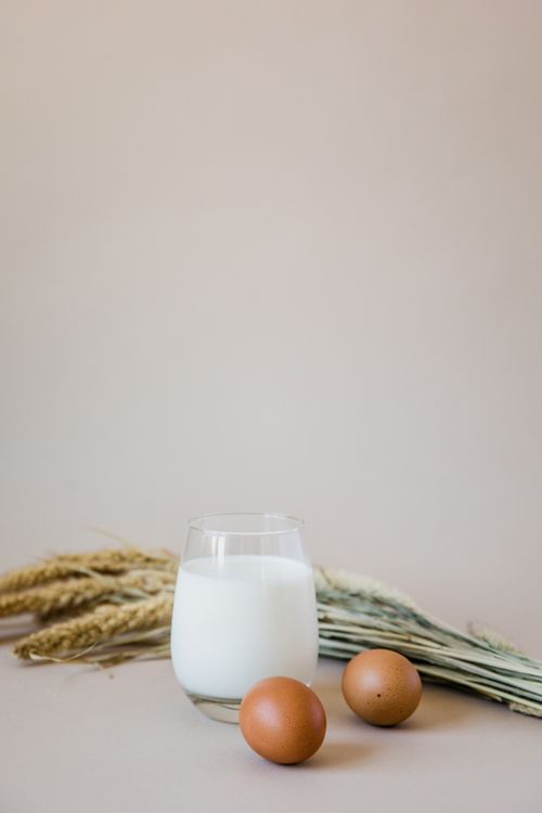 Free Glass of milk with eggs and wheat on a neutral background, showcasing nutritious essentials. Stock Photo