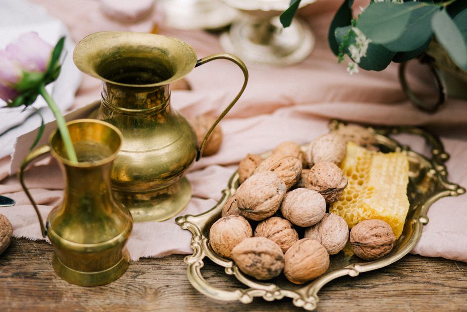 A rustic scene showcasing a brass jug, ripe walnuts, and fresh honeycomb on a decorative plate.