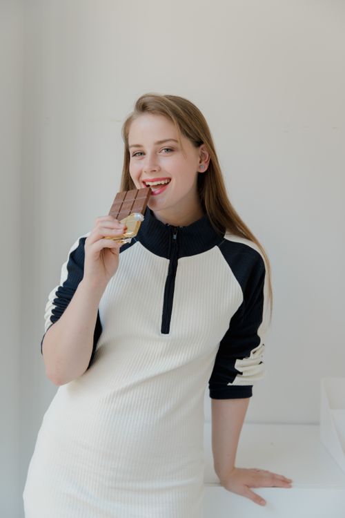 Free Smiling woman in a white dress enjoying a chocolate bar indoors. Stock Photo