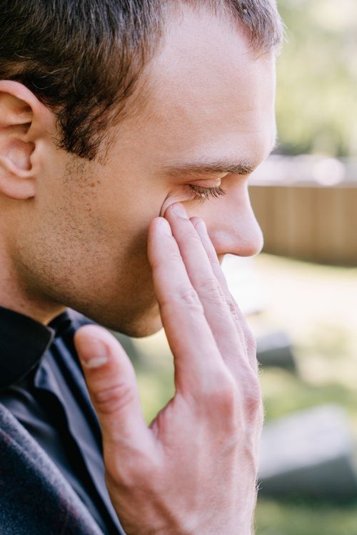 Free A pensive man holding his face in thought or sadness, set against an outdoor backdrop. Stock Photo