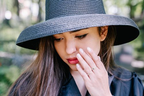 Free A thoughtful woman in a black hat with hand to face, outdoors. Stock Photo