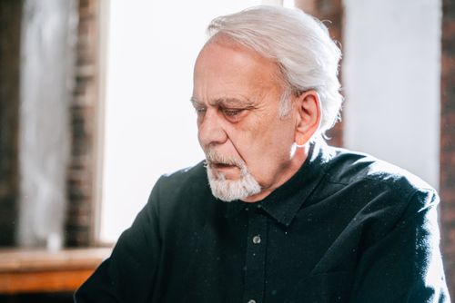 Free A senior man with white hair and a pensive expression, sitting indoors in soft lighting. Stock Photo