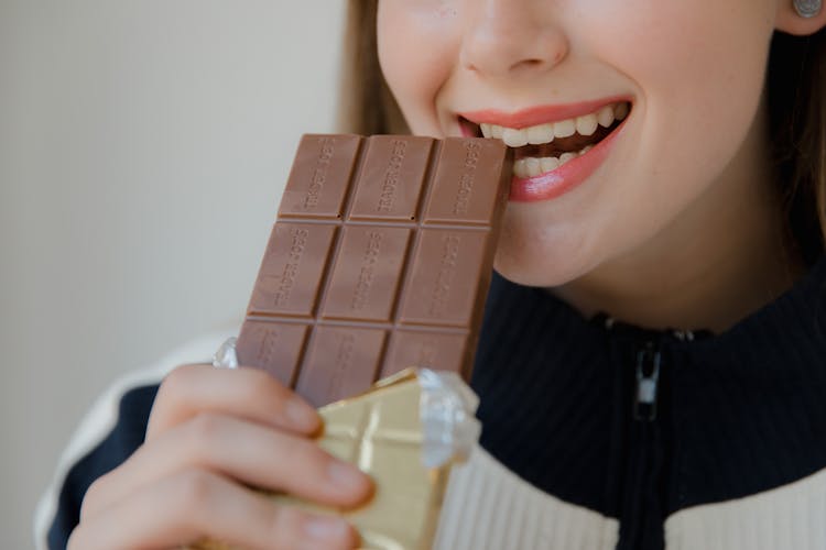 Woman Biting A Brown Chocolate Bar