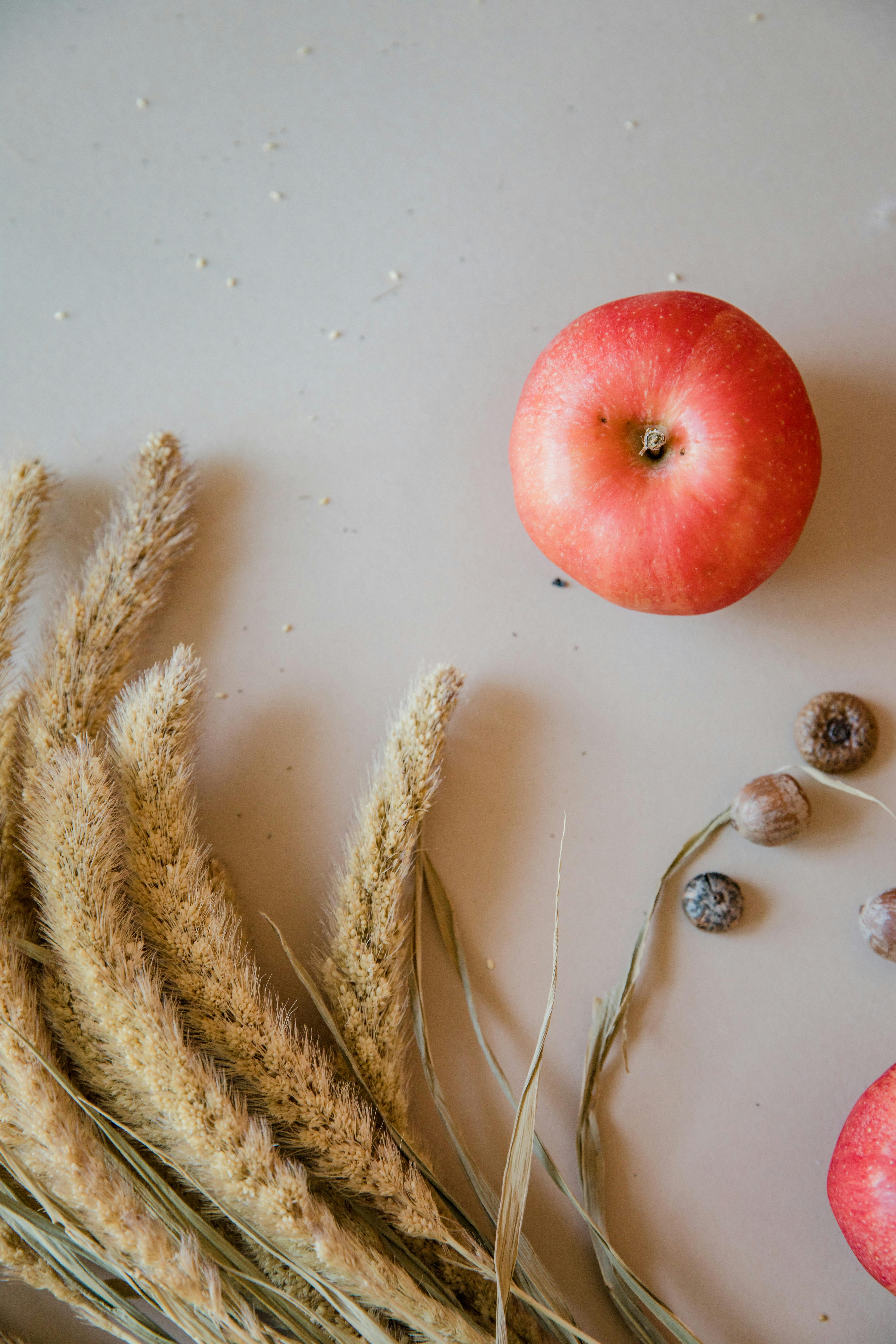 Flat lay composition with apple, dried wheat, and nuts on neutral background.
