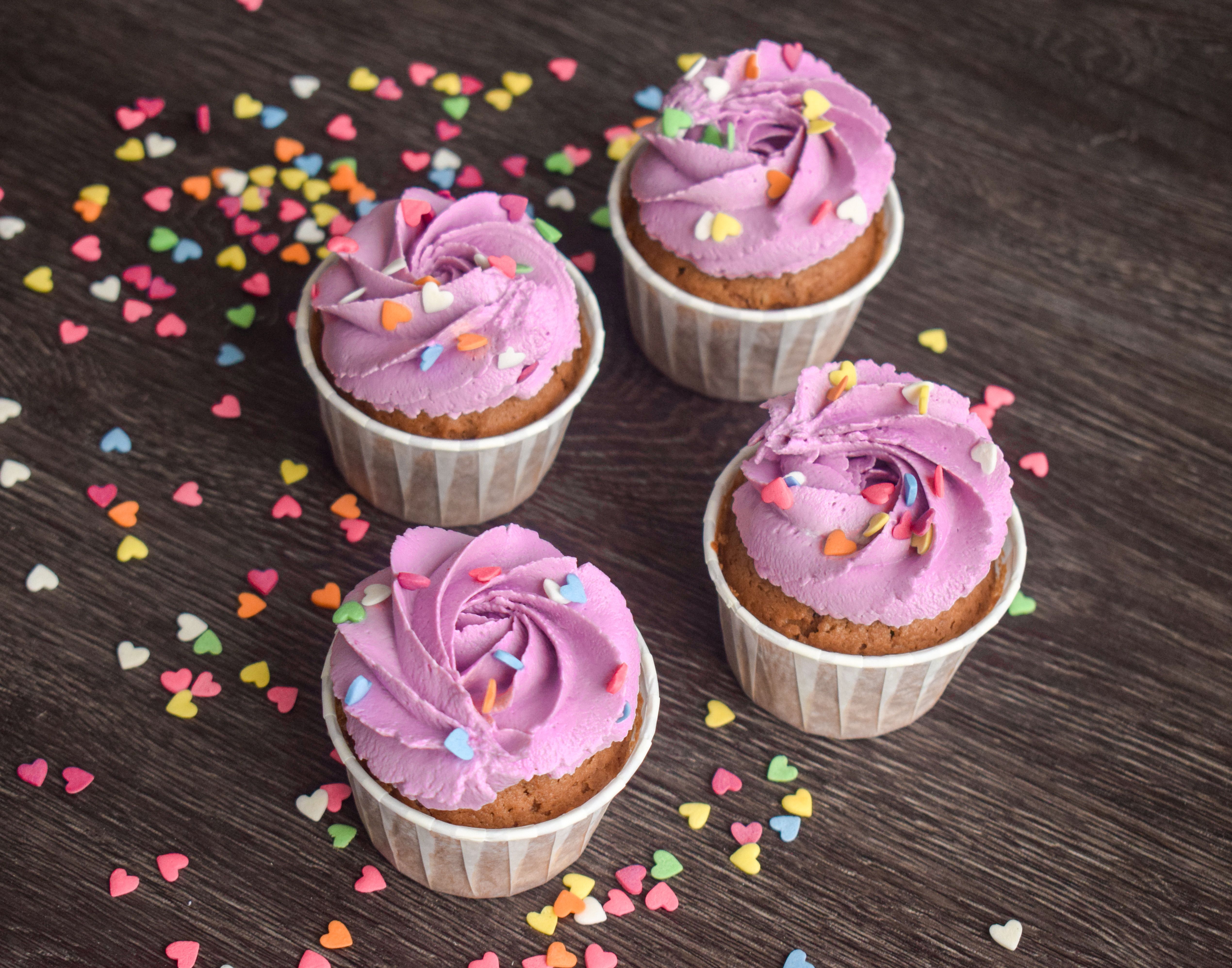Delicious cupcakes topped with purple frosting and vibrant heart sprinkles on a wooden surface.