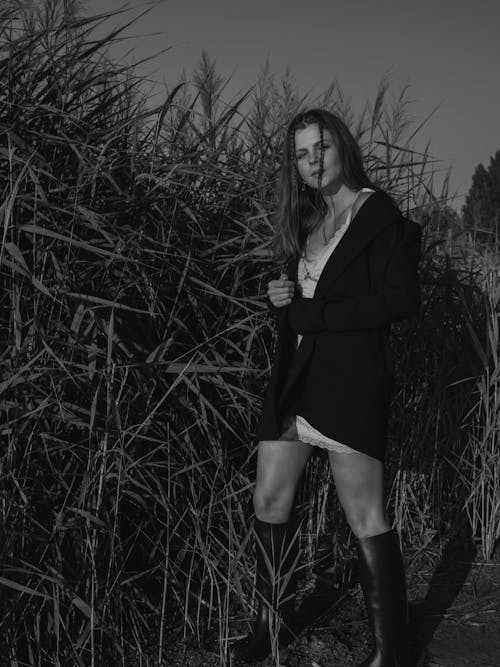 Grayscale Photo of a Woman in Black Blazer Standing near Tall Grass