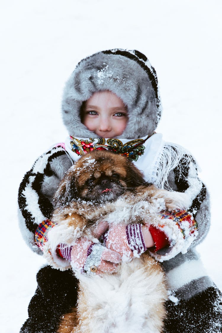 A Child In Winter Clothes Holding A Dog