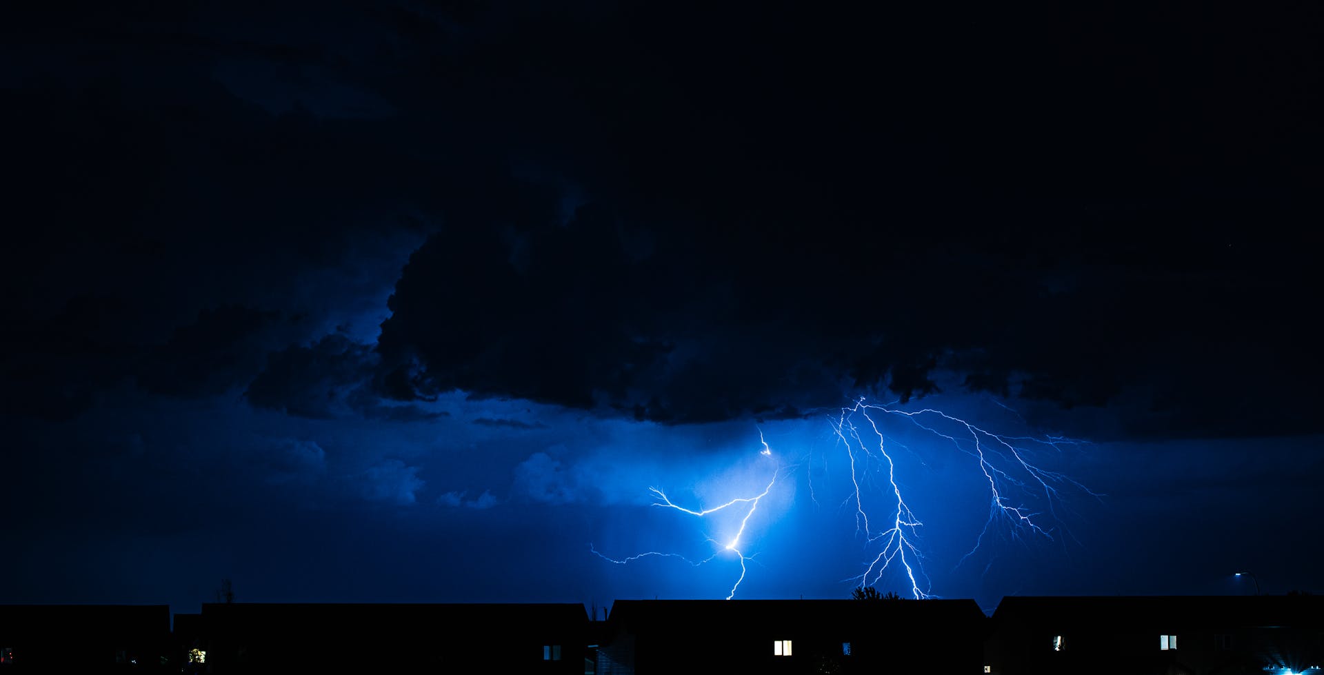 Powerful lightning illuminates the night sky during a storm, casting silhouettes over city rooftops.