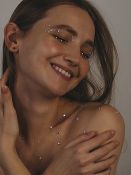 Close-up portrait of a smiling woman adorned with decorative face gems, eyes closed in contentment.