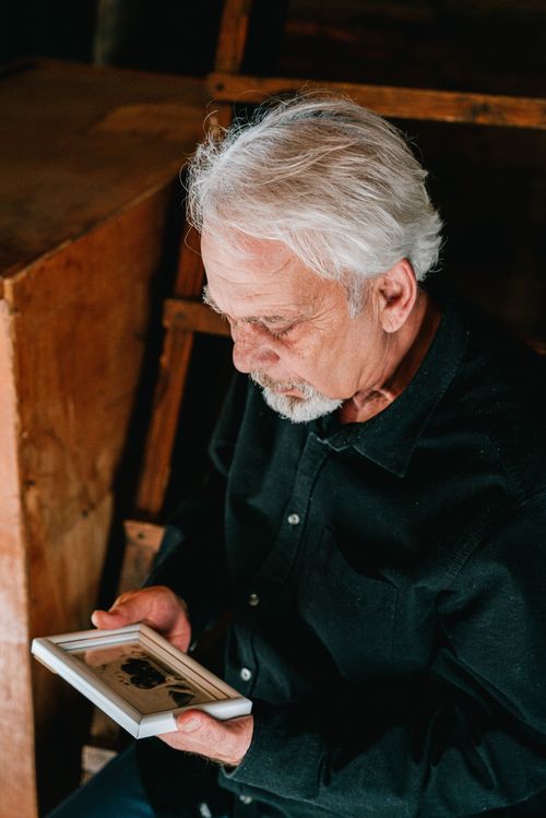 Free Senior man holding a photograph, deep in thought, evoking memories and emotion. Stock Photo