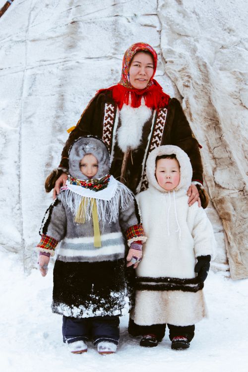 Free A family in traditional winter clothing stands outside a snow-covered dwelling. Stock Photo
