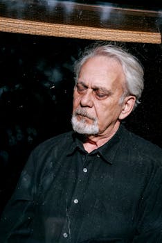 Portrait of an elderly man with white hair wearing a black shirt, deep in thought.