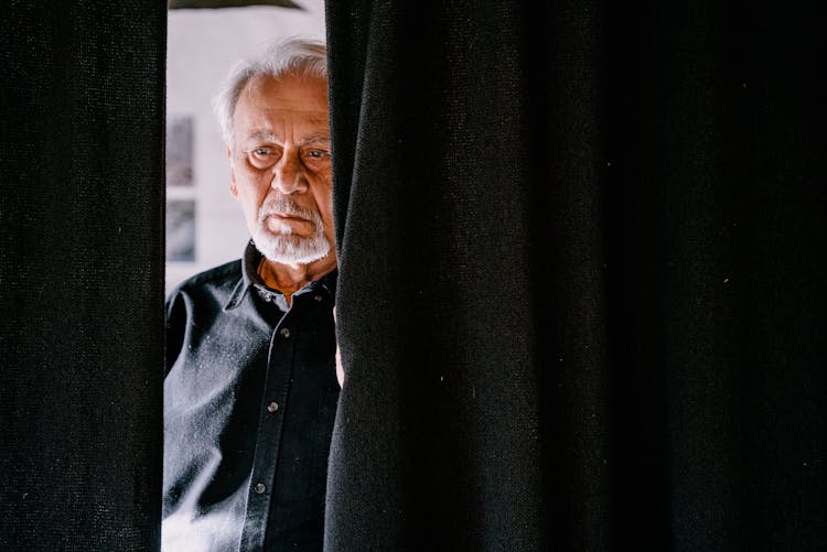 An Elderly Man Behind The Black Curtain