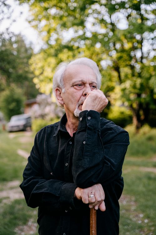 Free Senior man in a black shirt contemplating while leaning on a walking stick outdoors. Stock Photo