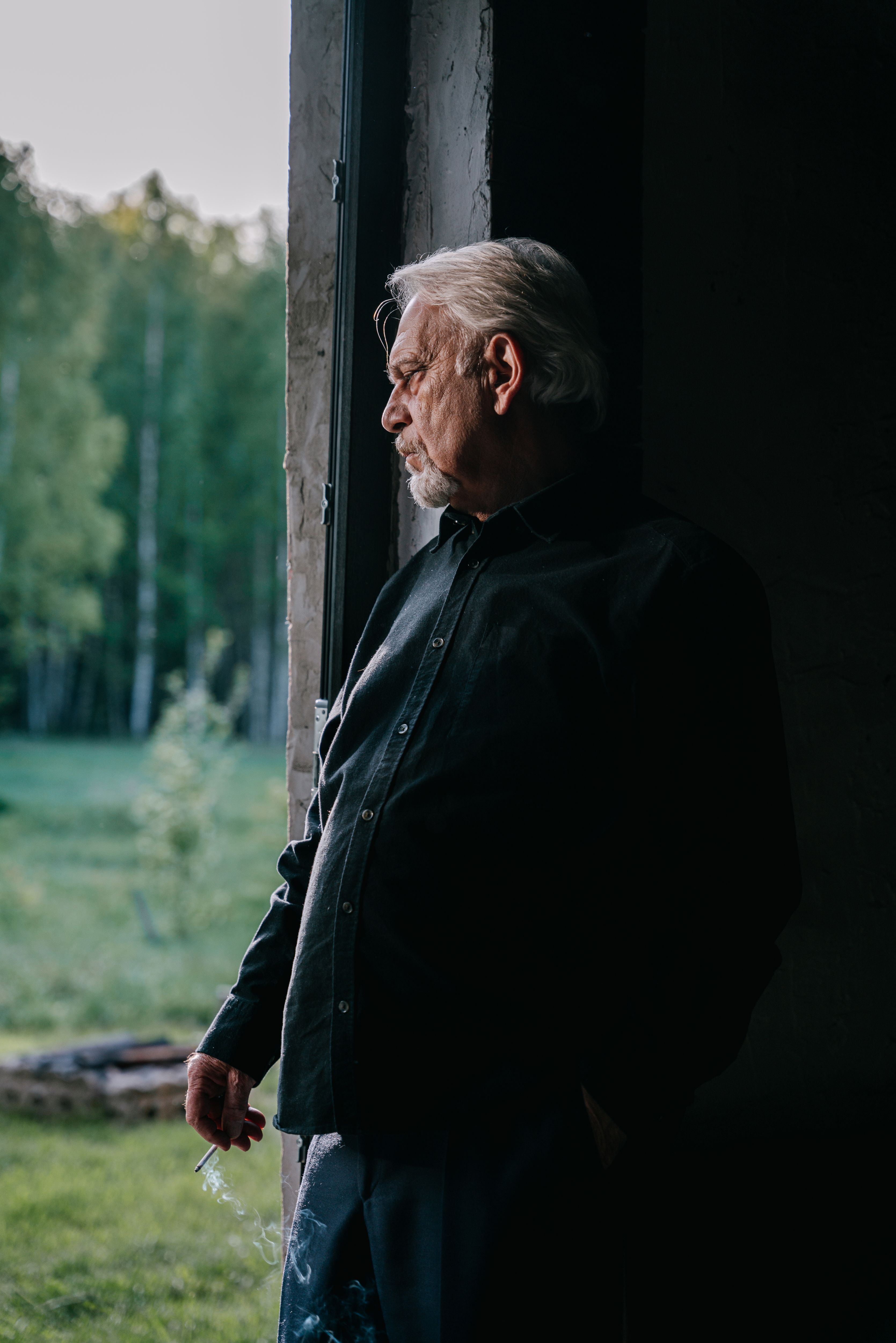 Elderly man with white hair looking out through a window. A contemplative moment captured indoors.