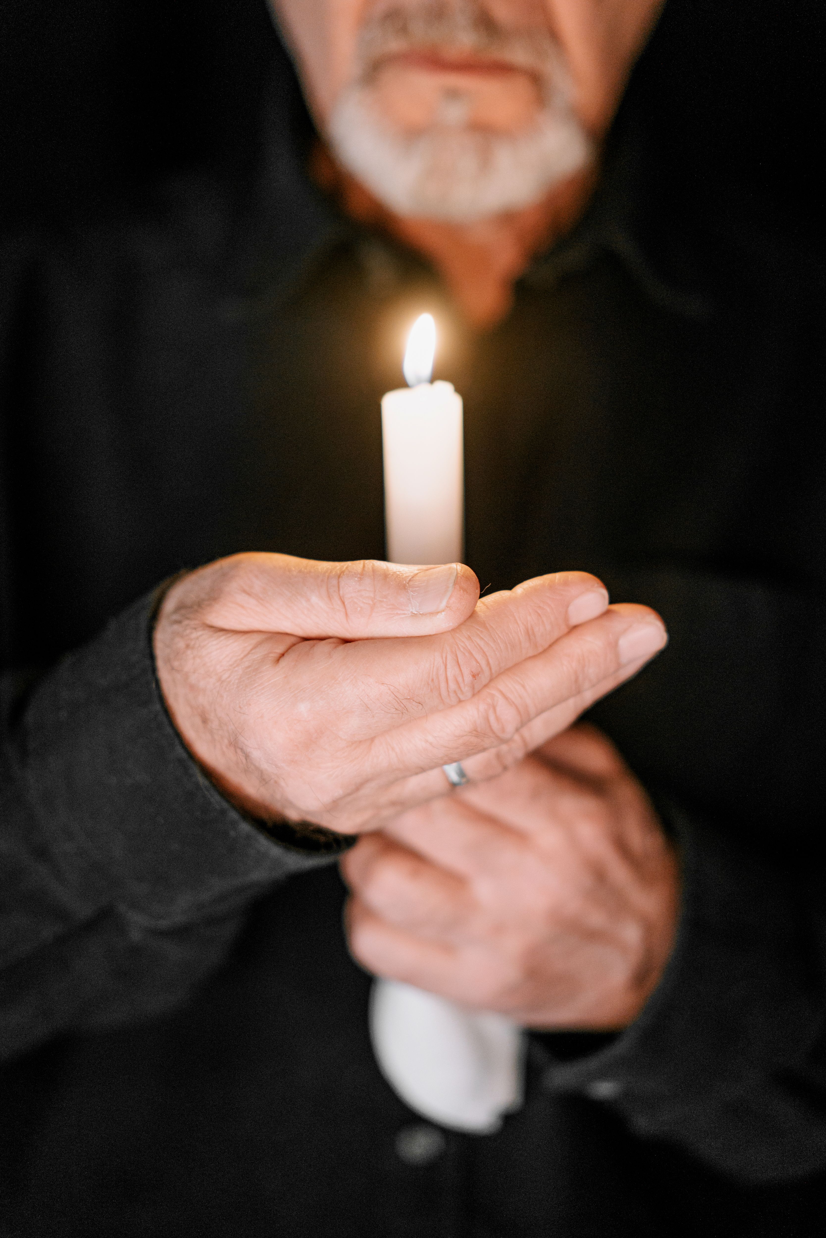 A man holding a lit candle against a dark background, symbolizing grief and reflection.