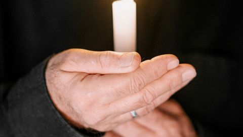 A man holding a lit candle against a dark background, symbolizing grief and reflection.