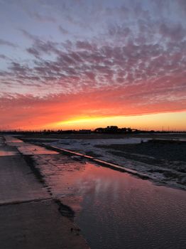 Stunning sunset reflects on icy puddles in a winter landscape, Novy Urengoy, Russia, creating a vivid sky pattern.