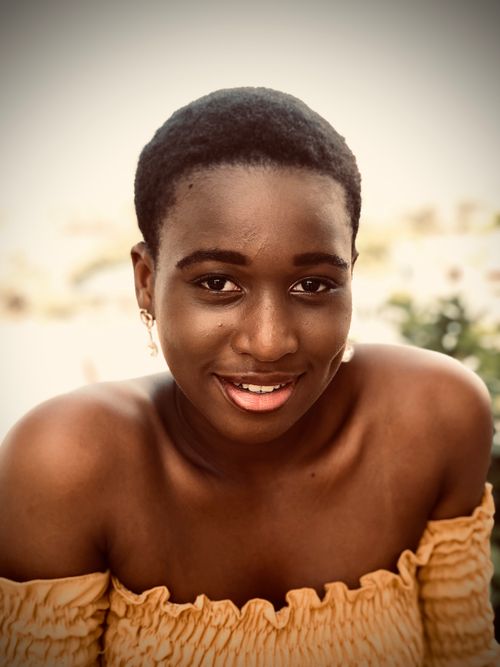 Free Cheerful portrait of a young woman in a yellow off-shoulder top, radiating warmth and elegance. Stock Photo
