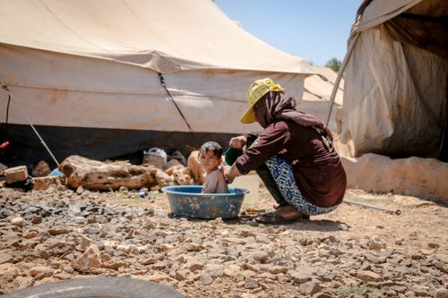 Free A mother bathes her child outdoors in a refugee camp in Idlib, Syria. Stock Photo