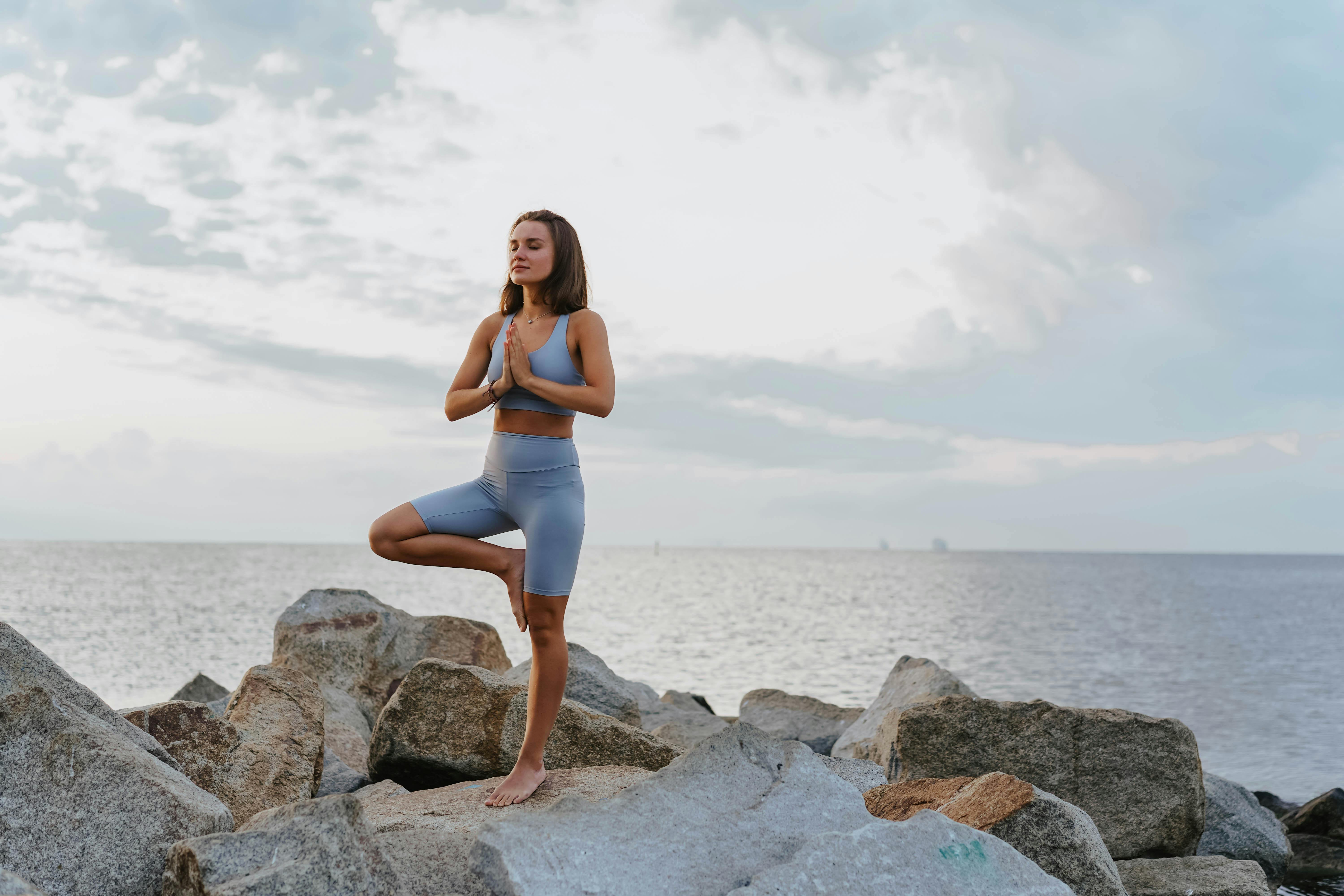 a woman doing a yoga exercise near the ocean during morning