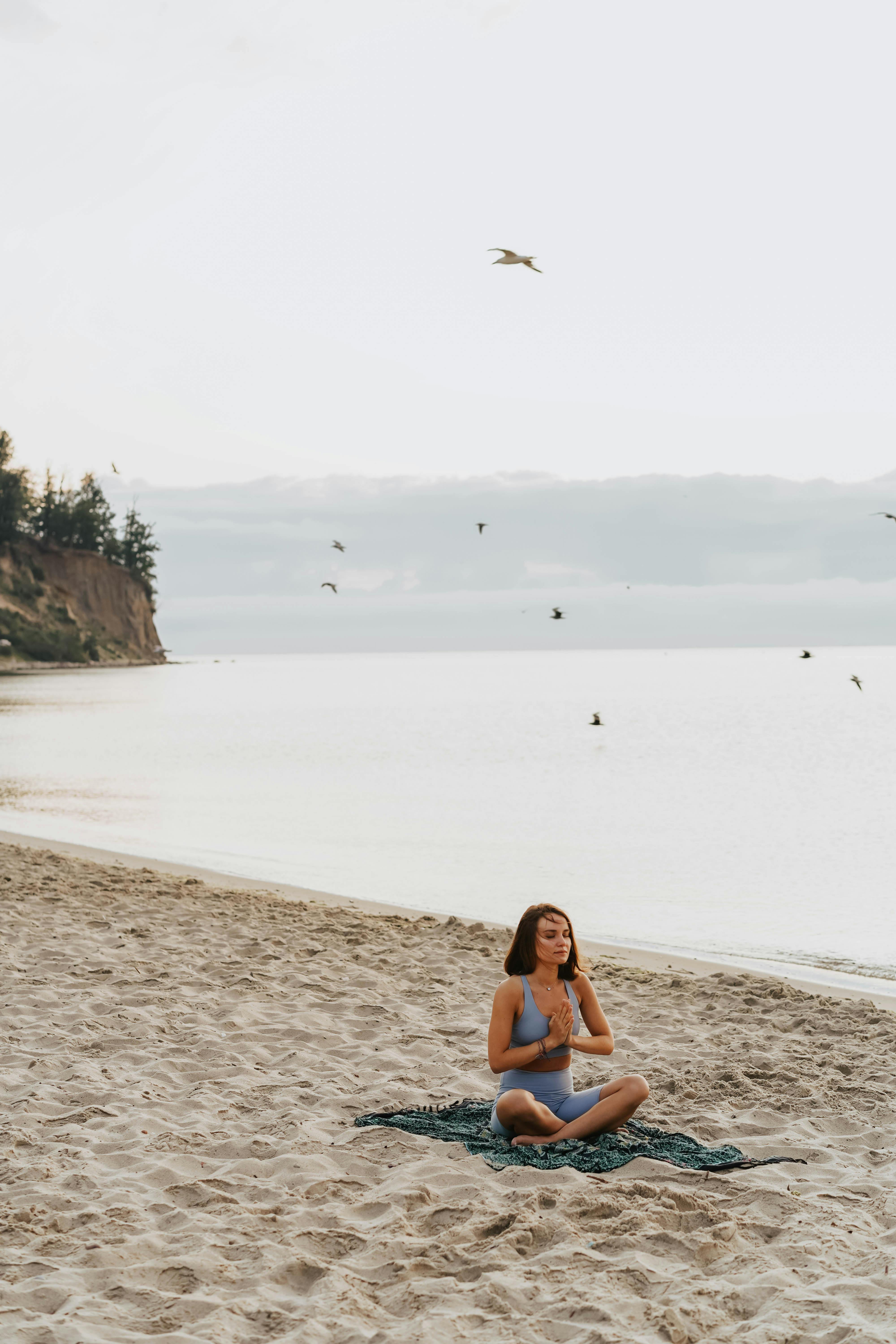 woman in blue top meditating on the beach near water