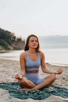 Young woman practicing yoga meditation on the beach at sunrise, promoting wellness and serenity.