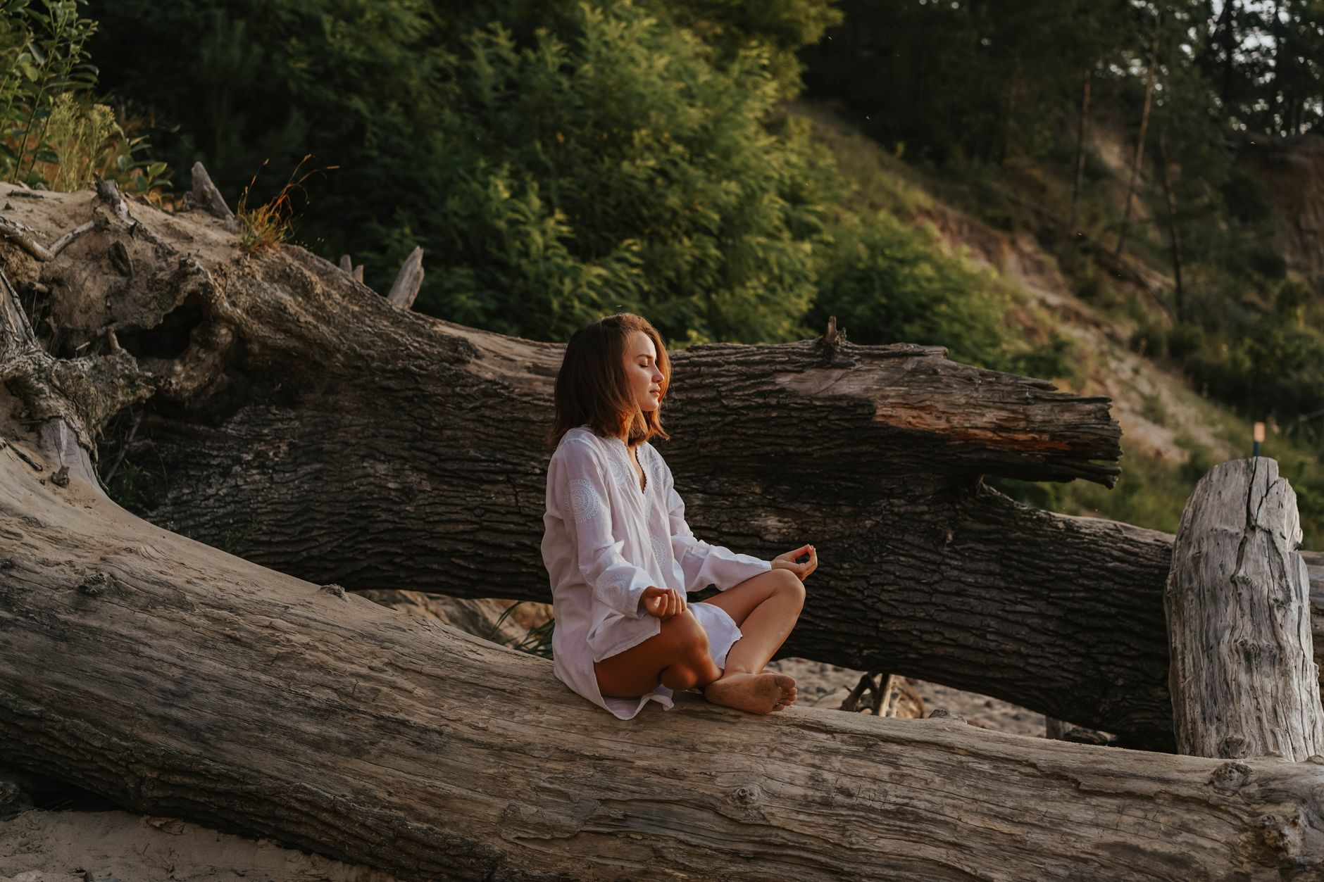 冥想提升睡眠品質:科學證據與實踐指南 Woman in white shirt meditates on a large log in a forest setting during the day.