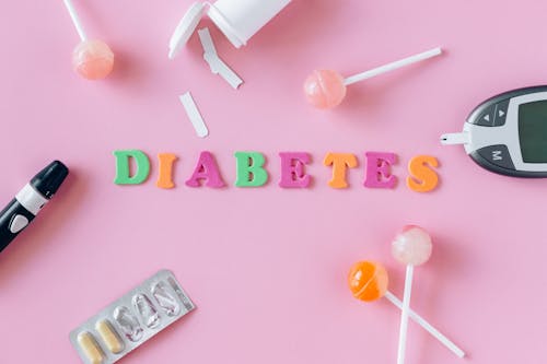 Word "Diabetes" Made of Colorful Letters Lying among Lollipops, Medication and Blood Sugar Monitor Devices 